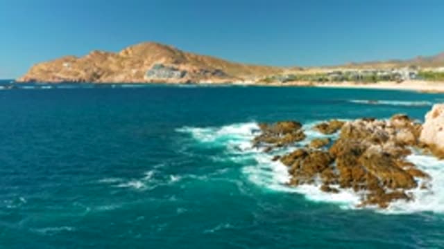 CHILENO BEACH LOS CABOS BCS MEXICO-2022: Waves Crashing Against Rocky Shoreline with Mountain Backdrop