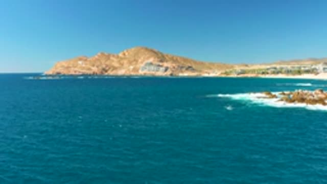 CHILENO BEACH LOS CABOS BCS MEXICO-2022: Ocean Waves Crashing Against Rocky Shore with Hill Backdrop