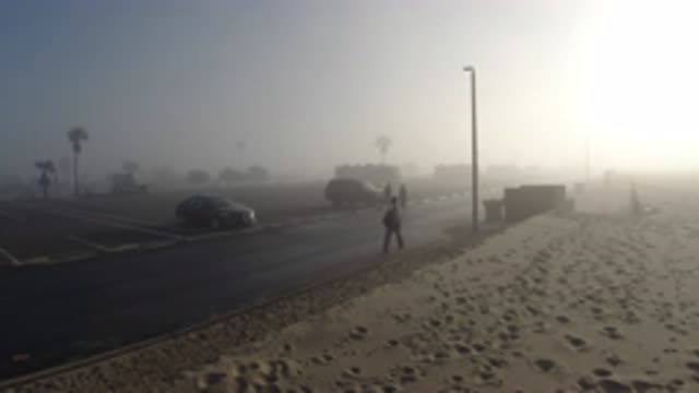 HUNTINGTON BEACH CALIFORNIA-2019: People Walk Along Road in Fog as Sun Rises Near Parking Lot