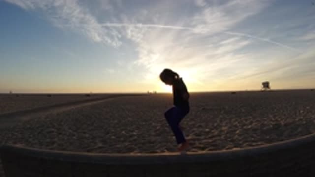 BOLSA CHICA CALIFORNIA-2019: Silhouette Of A Little Girl Jumping In Front Of A Tree At Sunset