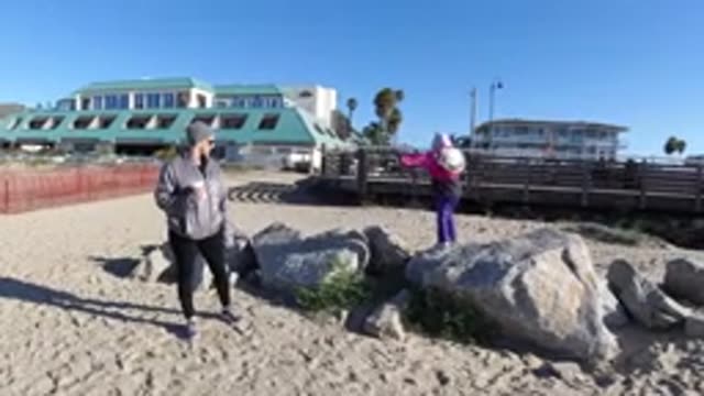 PISMO BEACH CALIFORNIA-2019: Girl Wearing Pink Jacket Stands On Large Grey Rocks