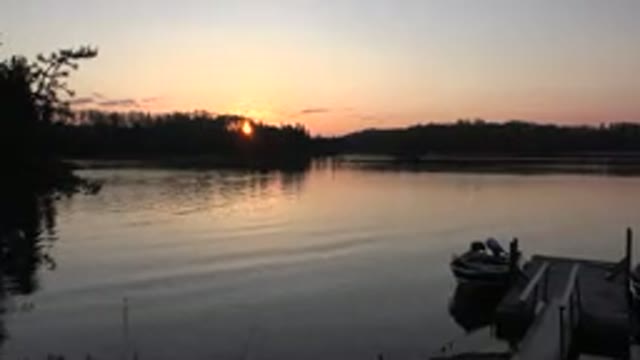 RED LAKE CANADA-2015: Pretty Orange Sky With Sun Behind Trees In Distance Boat