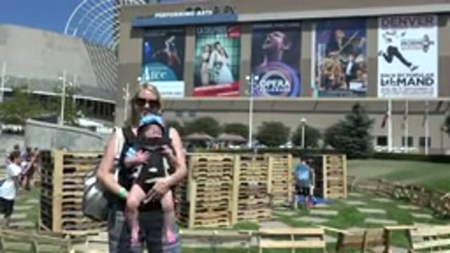 DENVER COLORADO-2015: Woman Wearing Black Shirt Holds Baby Wearing Blue Hat On A Sunny Day