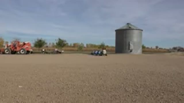 BRIGHTON COLORADO-2015: Small Tractor Towing a Series of Blue Tanks in a Dirt Field