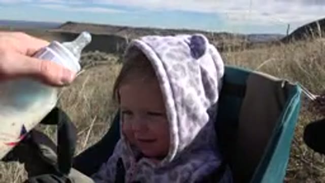 GOLDEN COLORADO-2015: Blond Baby Wearing Purple Cap Smiling While Holding a Bottle