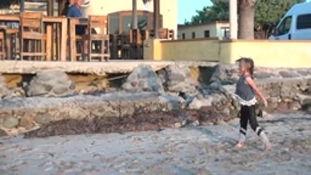 SAN CARLOS BCS MEXICO-2022: Child Playing on Sandy Beach with People in Background