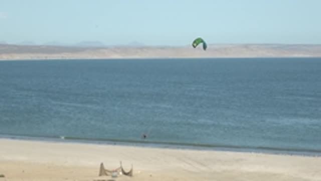 SAN JUANICO BCS MEXICO-2022: Kite Surfer Gliding on Ocean Near Sandy Beach