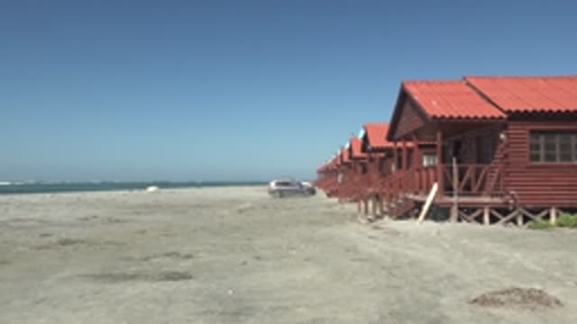 LA BOCANA BCS MEXICO-2022: Red-Roofed Cabins on Sandy Beach with Car Passing