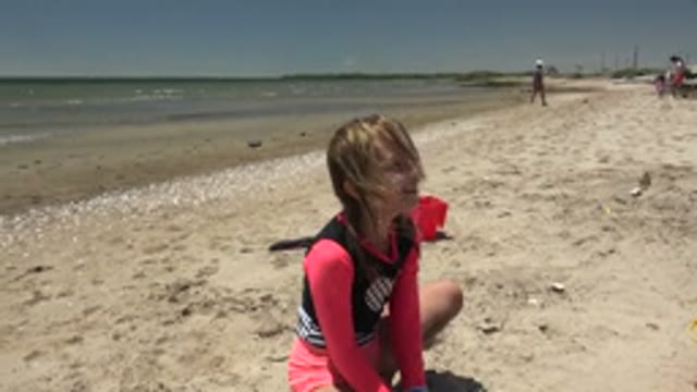 SAN CARLOS BCS MEXICO-2022: Girl Crouching on Sandy Beach Playing with Sand
