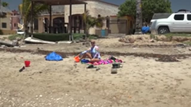 SAN CARLOS BCS MEXICO-2022: Beachgoer Relaxing on Towel Near Building and Truck