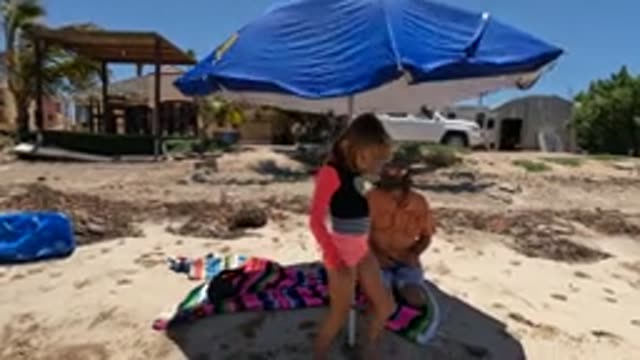 BAJA CALIFORNIA MEXICO-2022: Girl Moving Around Beach Under Blue Umbrella