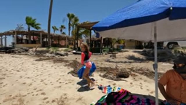 BAJA CALIFORNIA MEXICO-2022: Girl Carrying Blue Bag Across Sandy Beach