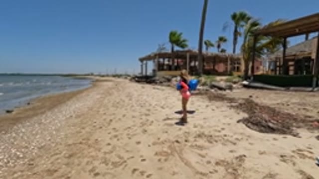 BAJA CALIFORNIA MEXICO-2022: Girl Dragging Blue Bag Along Sandy Beach
