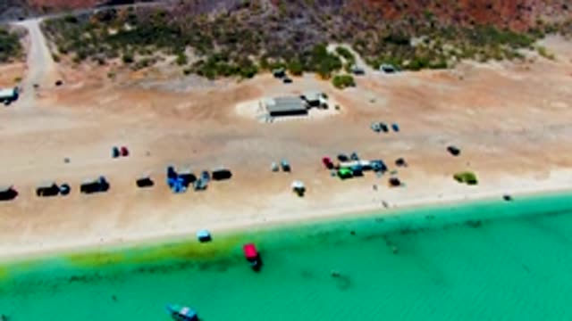PLAYA SANTISPAC BCS MEXICO-2022: Red Car Departing Sandy Beach by Turquoise Water