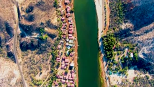 MULEGE BCS MEXICO-2022: Vehicle Moving Along Riverbank Road near Small Settlement
