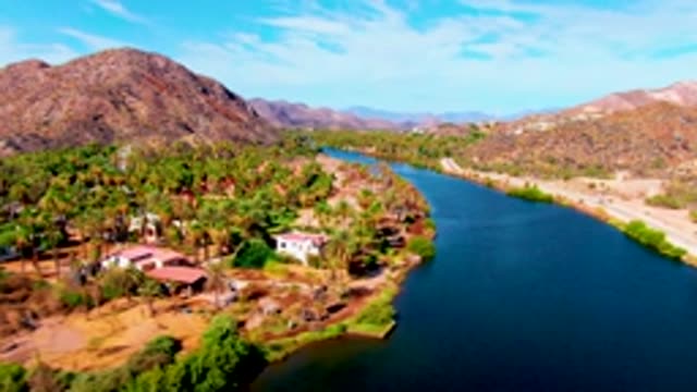 MULEGE BCS MEXICO-2022: Vehicle Moving Along Riverbank with Palm Trees and Mountains