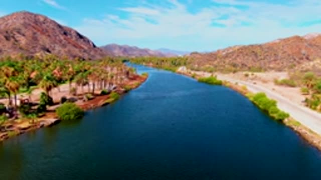 MULEGE BCS MEXICO-2022: Canal Flanked by Palm Trees and Road with Mountain Backdrop