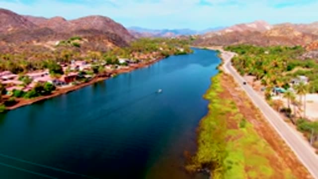 MULEGE BCS MEXICO-2022: Car and Boat Moving Along Lake Shore with Mountain Backdrop