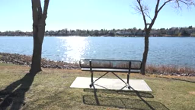 HIDDEN LAKE COLORADO-2017: Park Bench Near Trees Next To Shimmering Water On A