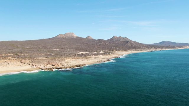 BUZZARDS BEACH EAST CAPE BCS MEXICO-2023: Waves Crashing on Sandy Shore with Distant Mountains