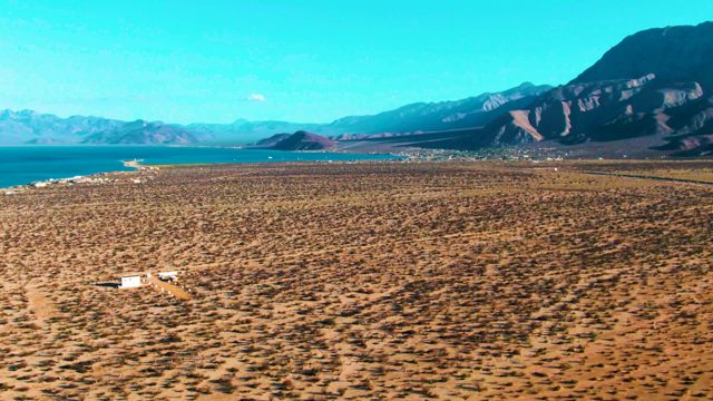 BAHIA DE LOS ANGELES BCS MEXICO-2022: Vehicle Travels Across Arid Plain with Distant Lake and Mountains