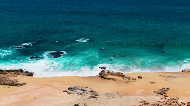 PUNTA BUZZARDS EAST CAPE BCS MEXICO-2022: Ocean Waves Crashing on Sandy Shore with Rocky Outcrops