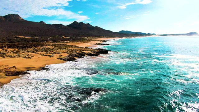 PUNTA BUZZARDS EAST CAPE BCS MEXICO-2022: Ocean Waves Crashing on Sandy Beach with Rocky Outcrops
