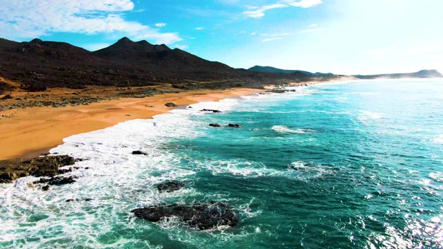 PUNTA BUZZARDS EAST CAPE BCS MEXICO-2022: Waves Crashing on Sandy Shore with Mountain Backdrop
