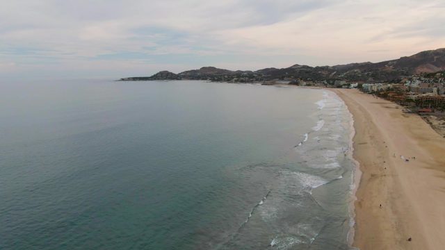 Waves Rolling Onto Sandy Shore with Distant Hills