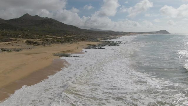PUNTA GORDO EAST CAPE BCS MEXICO-2022: Waves Rolling Onto Sandy Beach with Mountain Backdrop