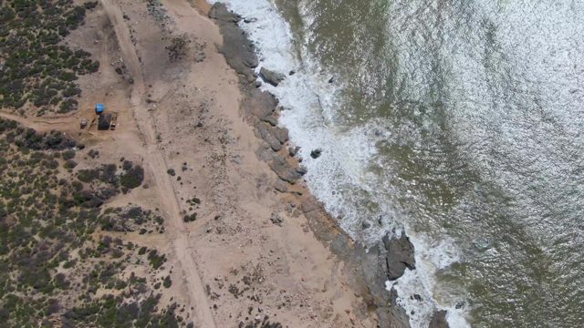BUZZARDS EAST CAPE LOS CABOS BCS MEXICO-2022: Waves Crashing on Rocky Shore with Sandy Beach and Dirt Road