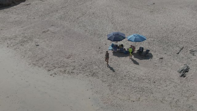 PLAYA EL ARBOLITO CABO PULMO BCS MEXICO-2022: Beachgoers Adjusting Under Umbrellas on Sandy Shore