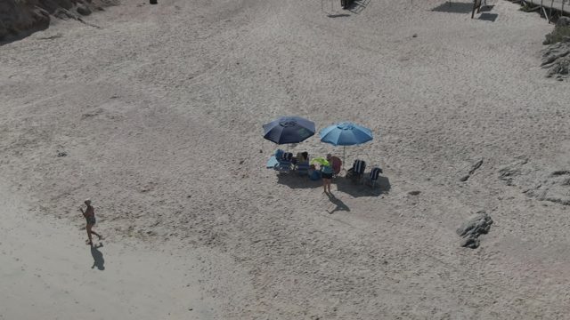 PLAYA EL ARBOLITO CABO PULMO BCS MEXICO-2022: Beachgoers Relaxing Under Umbrellas As a Person Walks By