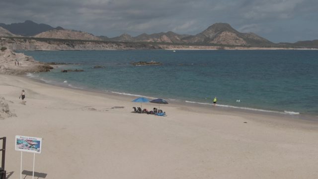 PLAYA EL ARBOLITO CABO PULMO BCS MEXICO-2022: Sandy Beach with Signboard, People, and Calm Ocean