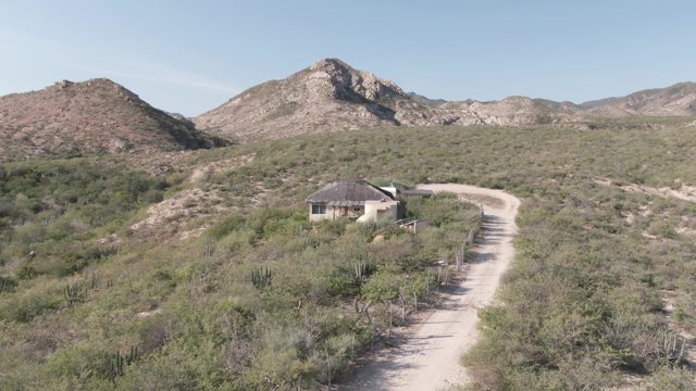CABO PULMO BCS MEXICO-2022: Desert Road Leading to a Small Building with Mountain Backdrop