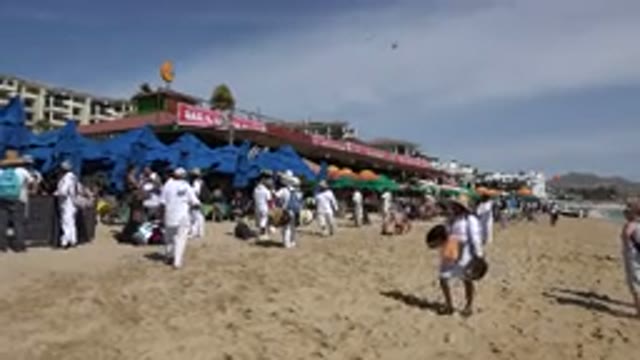 CABO SAN LUCAS MEXICO-2017: A Woman Among A Crowd Of People Walking Down The Beach