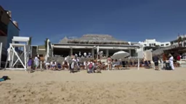 CABO SAN LUCAS MEXICO-2017: Street Vendor Wearing A Hat And Backpack In A Crowded Beach Area