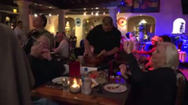 LOS CABOS MEXICO-2017: An Old Couple Records A Show While Their Waiter Prepares