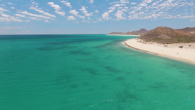 Sandy Beach and Turquoise Ocean with Scattered Clouds