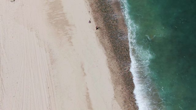 People Walking Along Sandy Shore with Ocean Waves