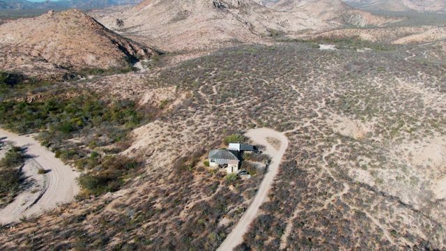 Car Traveling on Desert Road Past House