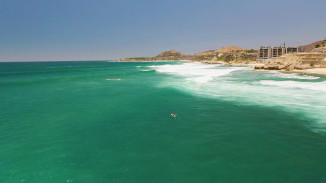 Person Swimming in Turquoise Ocean Near Rocky Coast