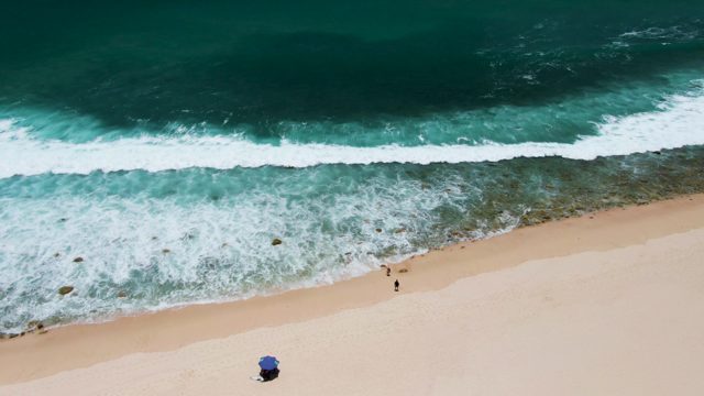 Beachgoers Walking Along Shoreline with Rolling Waves
