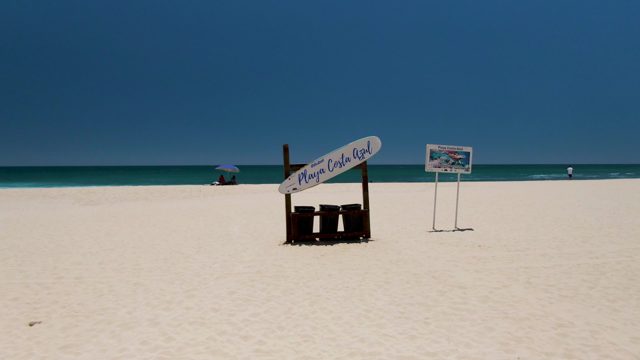 Beach with Sign and Distant Figures Moving