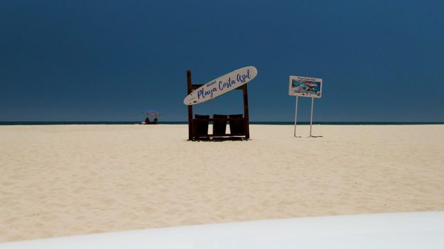 Person Walking on Sandy Beach Near Sign
