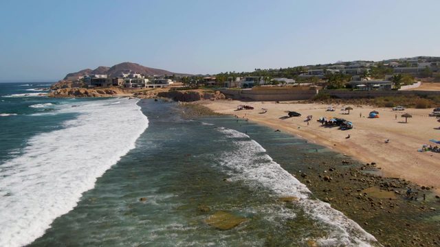 Waves Crashing on Sandy Beach with People and Vehicles
