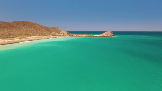 Gentle Ocean Waves at a Sandy Beach with Rocky Hills