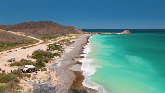 Sandy Beach with Turquoise Waves and Coastal Road