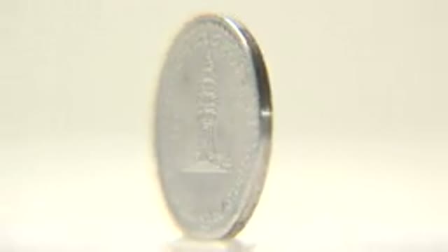 Close Up Of Rotating Silver Coin With Writing On One Side And A Building On The