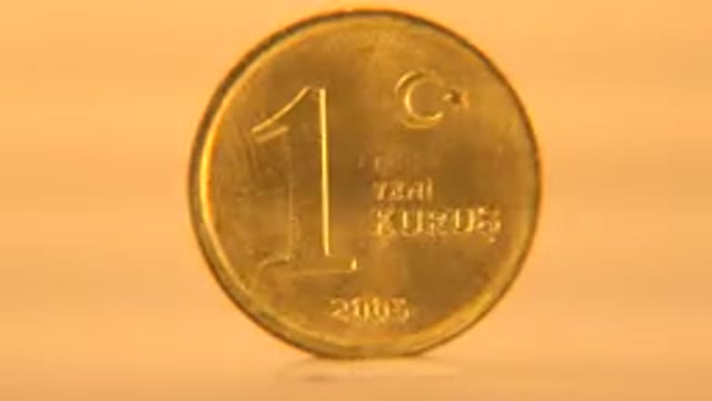 Gold Pound Coin Slowly Spinning On A Cream White Background